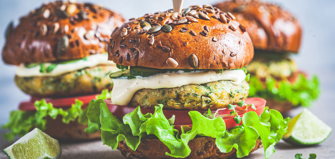 Vegan falafel burger with vegetables and sauce, dark background.