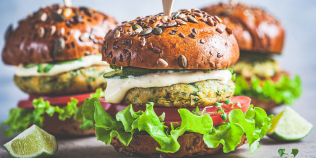 Vegan falafel burger with vegetables and sauce, dark background.